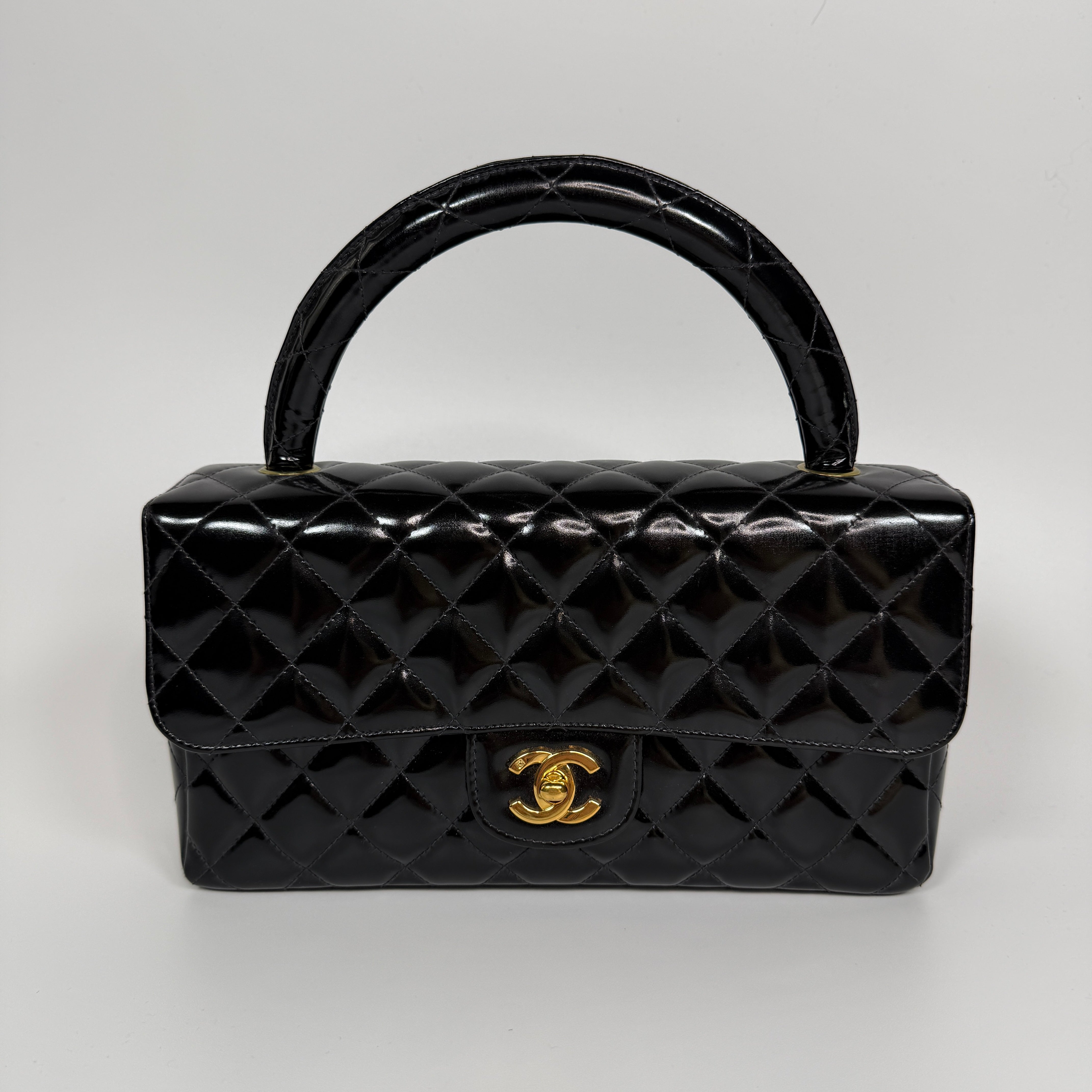Authentic and preloved Chanel Vintage Kelly Top Handle Bag In Black Patent Leather With 24kt Gold Hardware. Very Good condition. 100% Authenticity guarantee