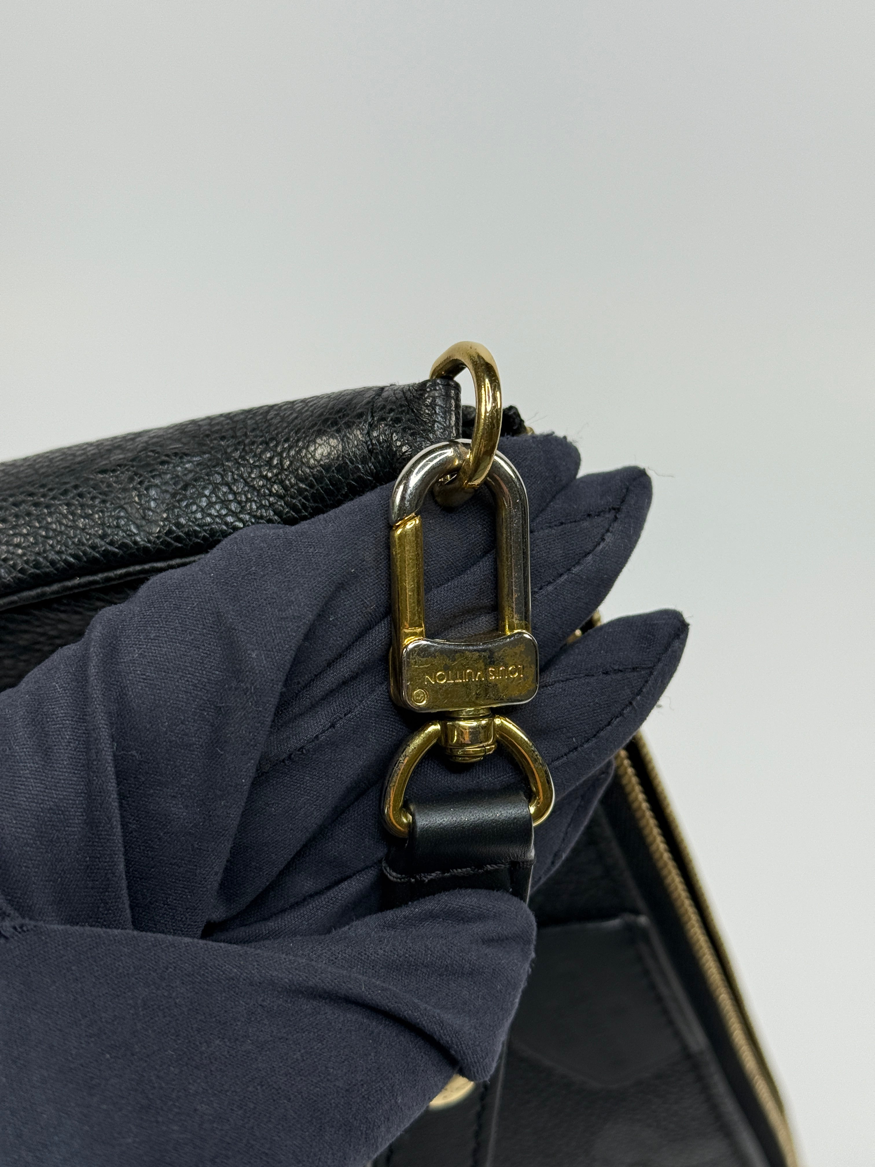 Close-up of a black handbag with a gold clasp on a light gray background