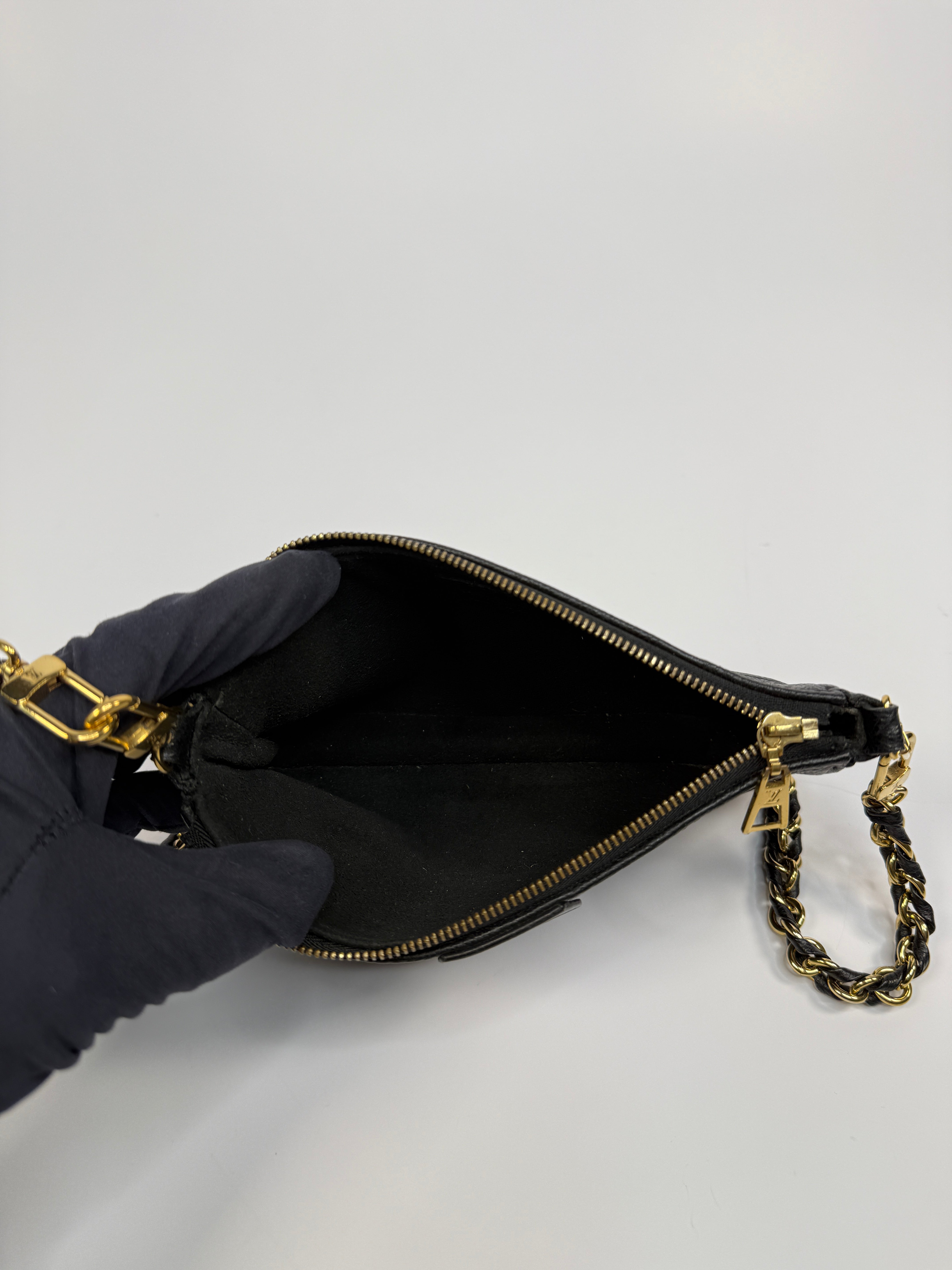 Black handbag with gold chain handle held by a gloved hand on a light gray background