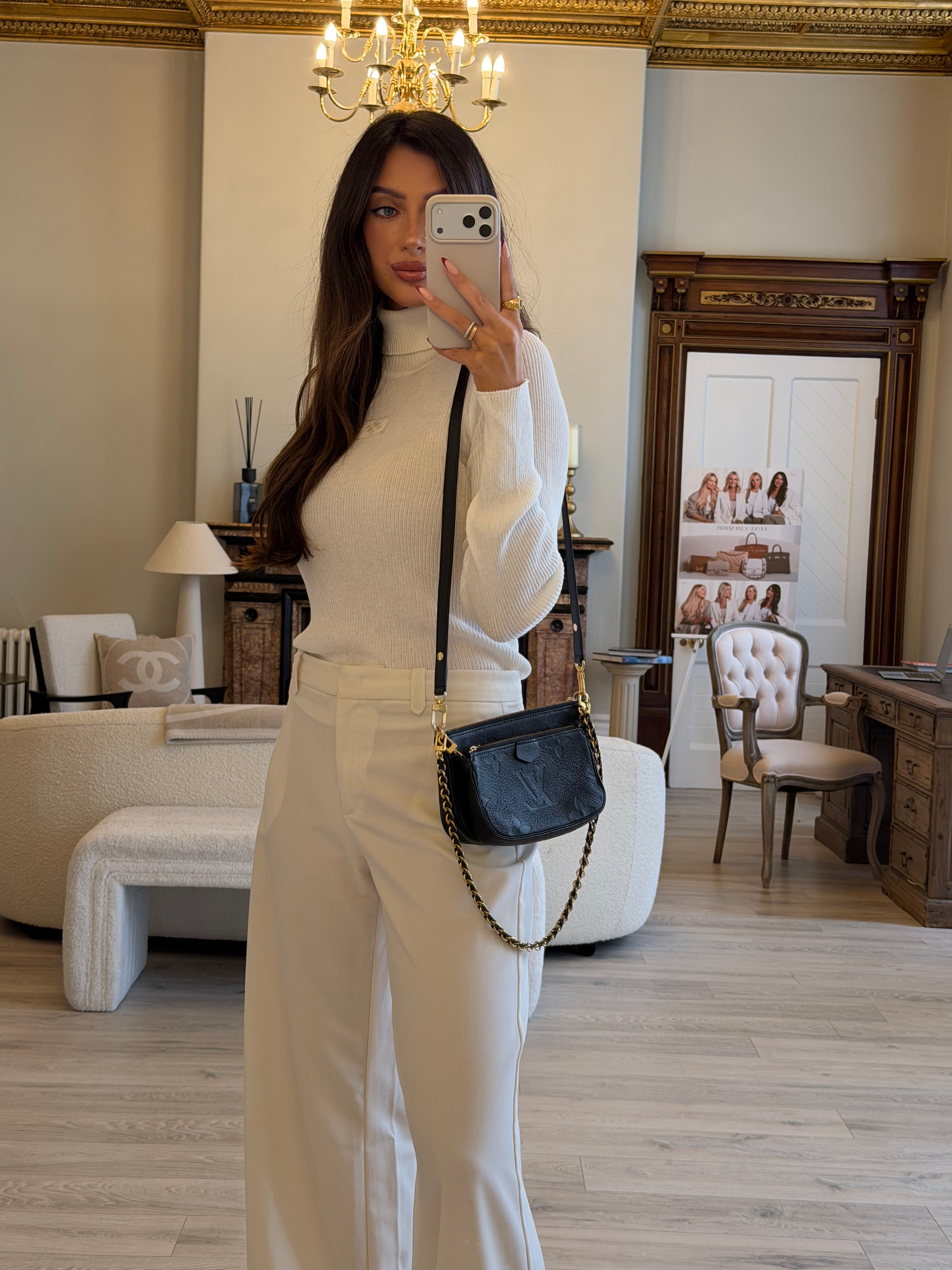 Woman taking a mirror selfie in an elegant room with a mirror and chair.