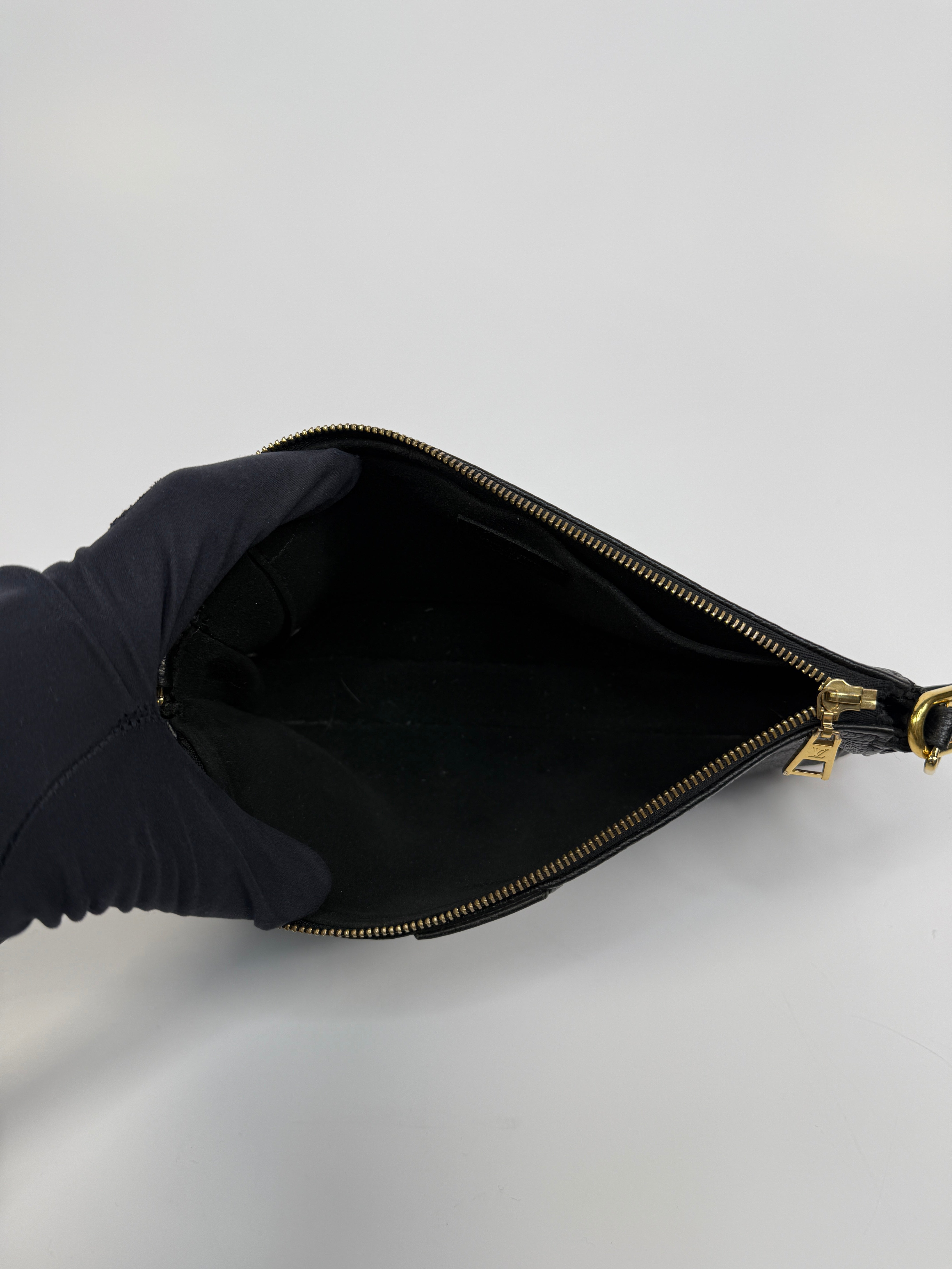 Black handbag held open by a gloved hand against a light gray background